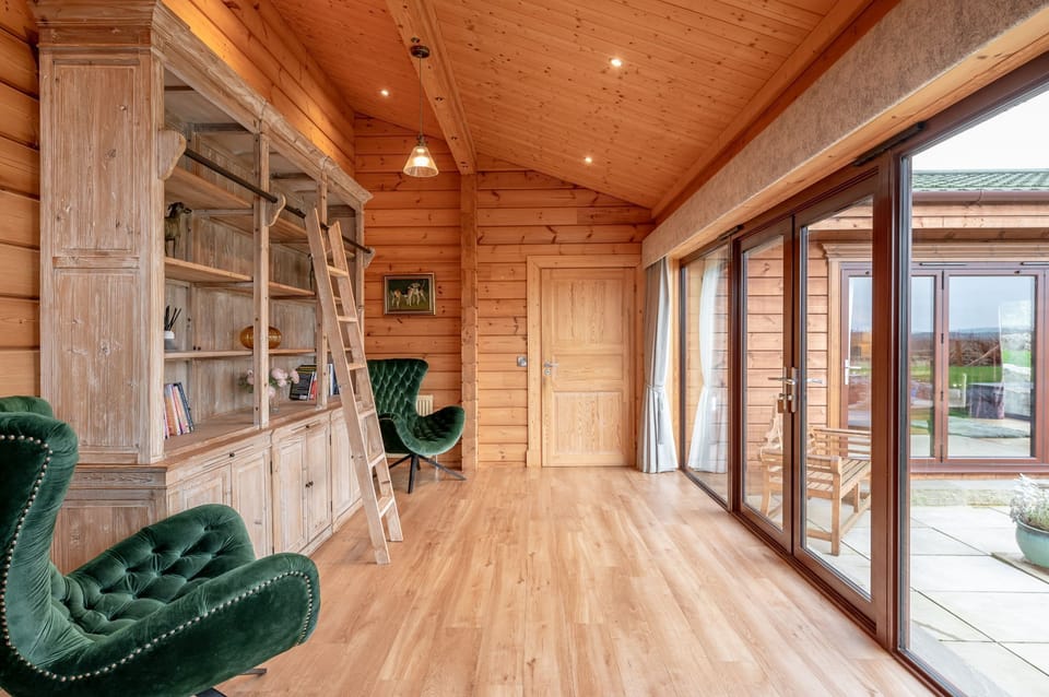 Reading area at Valley View with built-in wooden bookshelf, ladder and green velvet armchairs.