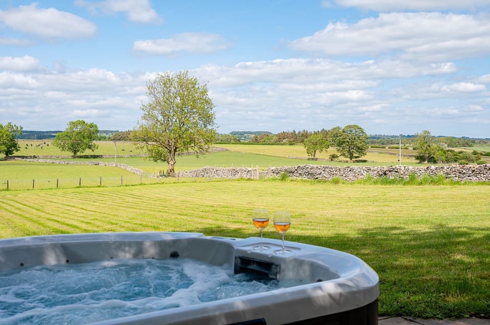 Bearskin hot tub area with privacy fencing and a field, set alongside the cottage.
