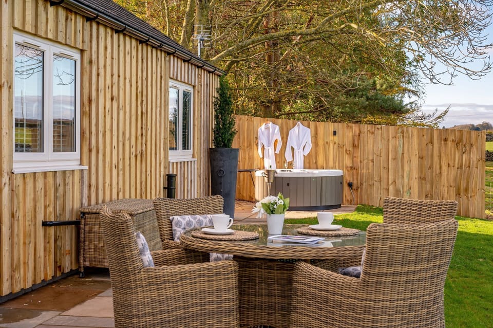 Bearskin patio seating area with wicker table and chairs on paving, with a hot tub.