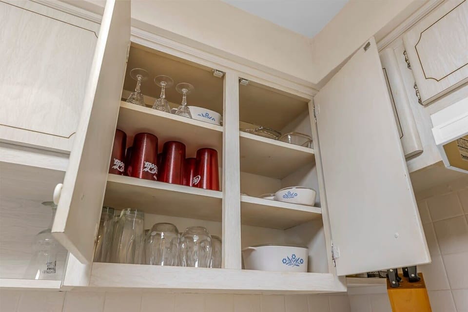 Open kitchen cabinet showing glassware and vintage dishware for guest use.
