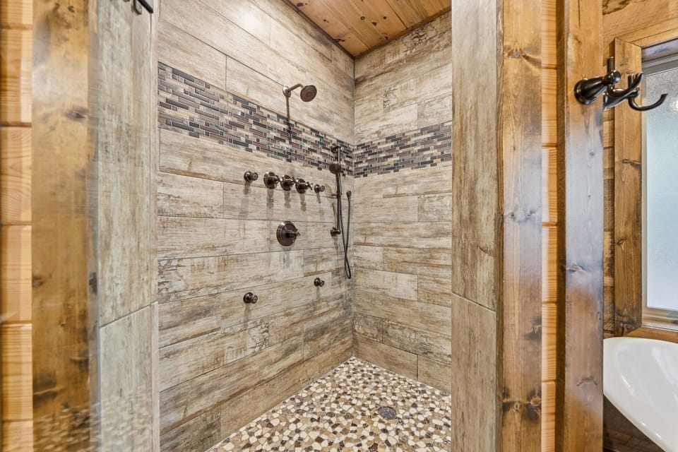 Walk-in tiled shower with multiple showerheads and pebble floor.