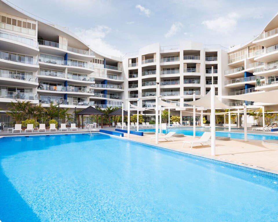 Wide shot of the resort pool area with sun lounges and the modern apartment buildings.