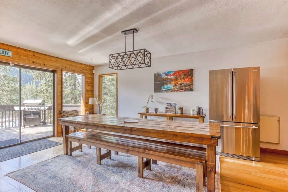 Adjacent to the kitchen, the spacious dining area holds a large wooden farmhouse table with benches under a lovely hanging woodland-style light fixture.