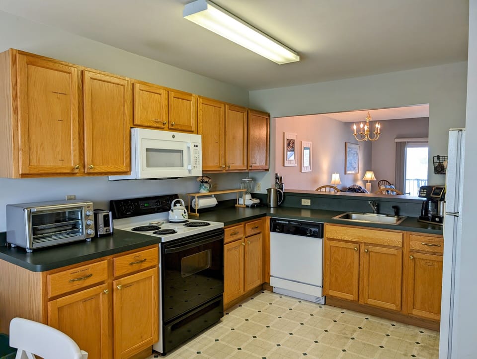 605 Crowley Drive - Efficient Kitchen with Ample Cabinetry - The kitchen offers a practical layout with warm wood cabinets and extensive black countertops for meal preparation. Modern appliances, including a built-in microwave and dishwasher, make this space move-in ready for vacation or permanent living.