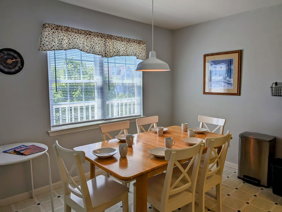 605 Crowley Drive - Sunlit Kitchen Dining Nook - A cozy breakfast area is nestled beside large windows, providing a bright spot for morning meals. The space features a classic wooden table and chairs, accented by soft coastal window treatments.