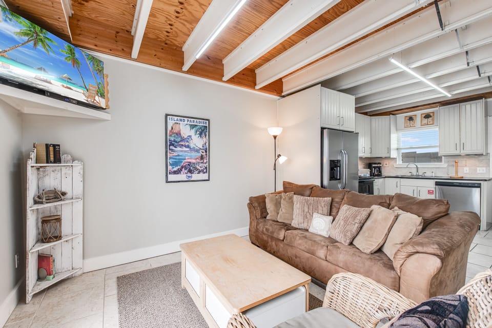 Relax on your plush sectional sofa beneath stunning exposed wood beam ceilings, where coastal art and modern amenities create your perfect home base.