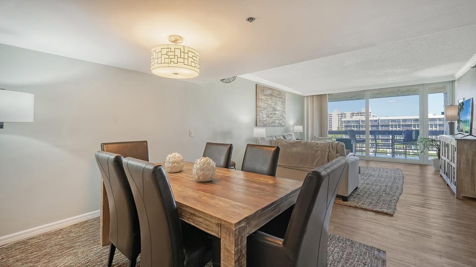 Six dark leather dining chairs surround a sturdy reclaimed wood table under a patterned drum light.
