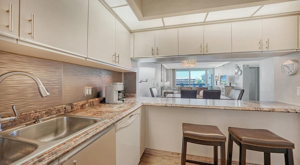 Granite countertops extend to a breakfast bar with two leather stools, overlooking the living room and balcony.