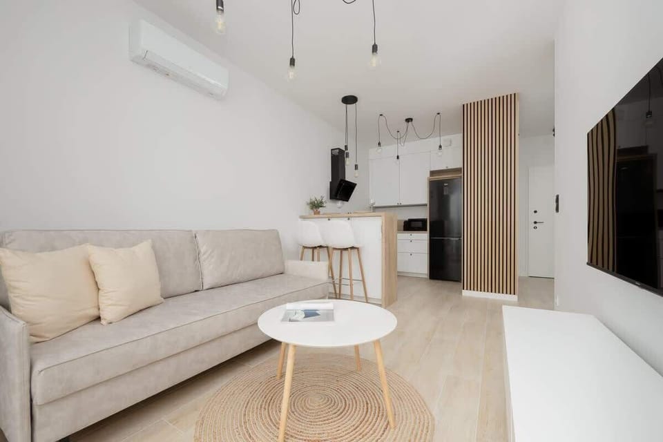 A welcoming living room with a beige sectional sofa, light wooden floors, and large windows. The perfect place to unwind or enjoy a movie night.