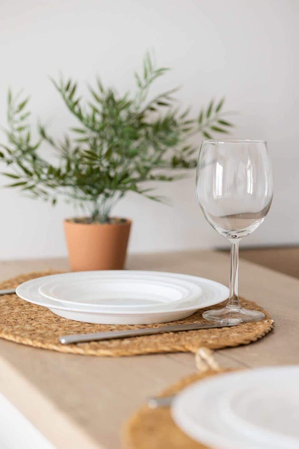 A close-up of a dining area with a small plant and a wine glass on a wooden table. A calming, simple setup for a meal or quiet moment.