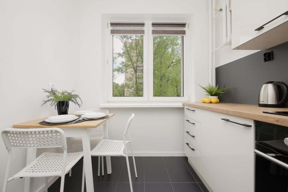 A dining area with a small white table and two chairs next to a bright window. Greenery outside the window adds a fresh touch.
