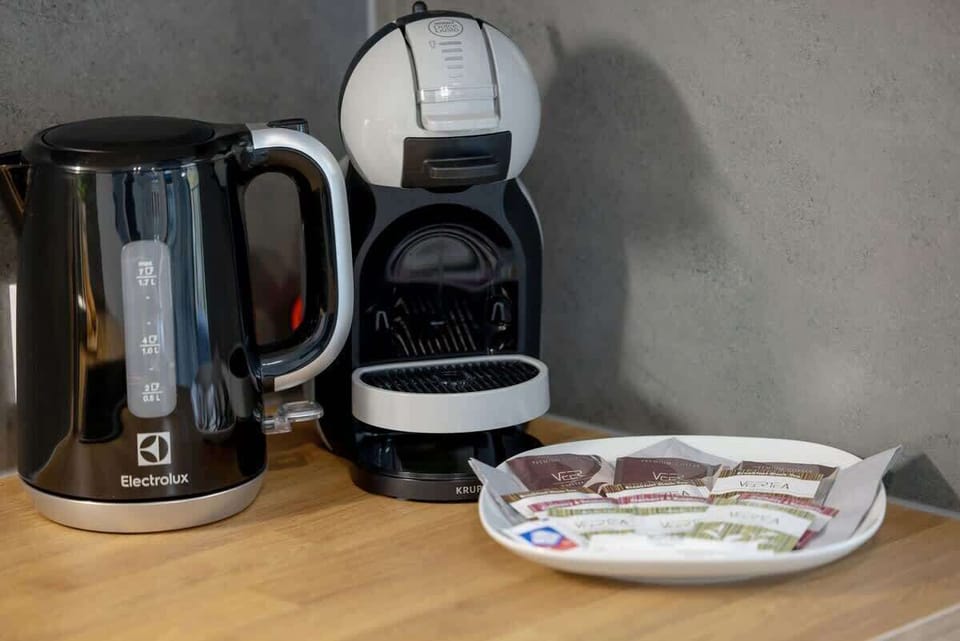 A close-up of a coffee station with a coffee maker, cups, and a tray of snacks, possibly set up on a kitchen counter.