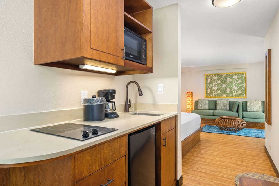 Your fully equipped kitchenette features modern appliances and warm wood cabinetry, opening seamlessly to a bright living space where you can unwind on the inviting green sofa after a day of exploring.