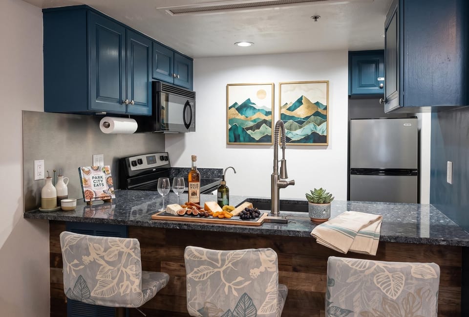 Dark blue cabinets frame the kitchen with granite counters, floral-patterned bar stools, and mountain artwork.