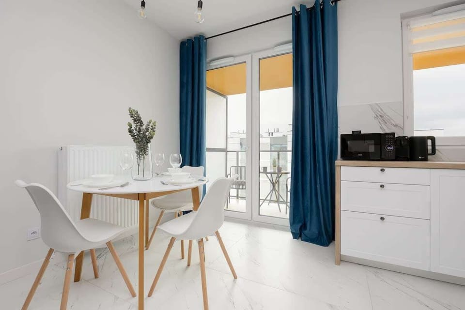 A sleek dining area with a white table and four chairs, next to a fully equipped kitchenette. The space combines functionality and style.