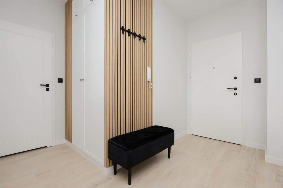 A hallway view with a white entrance door, wooden panels, and a black bench. Clean, organized, and welcoming.