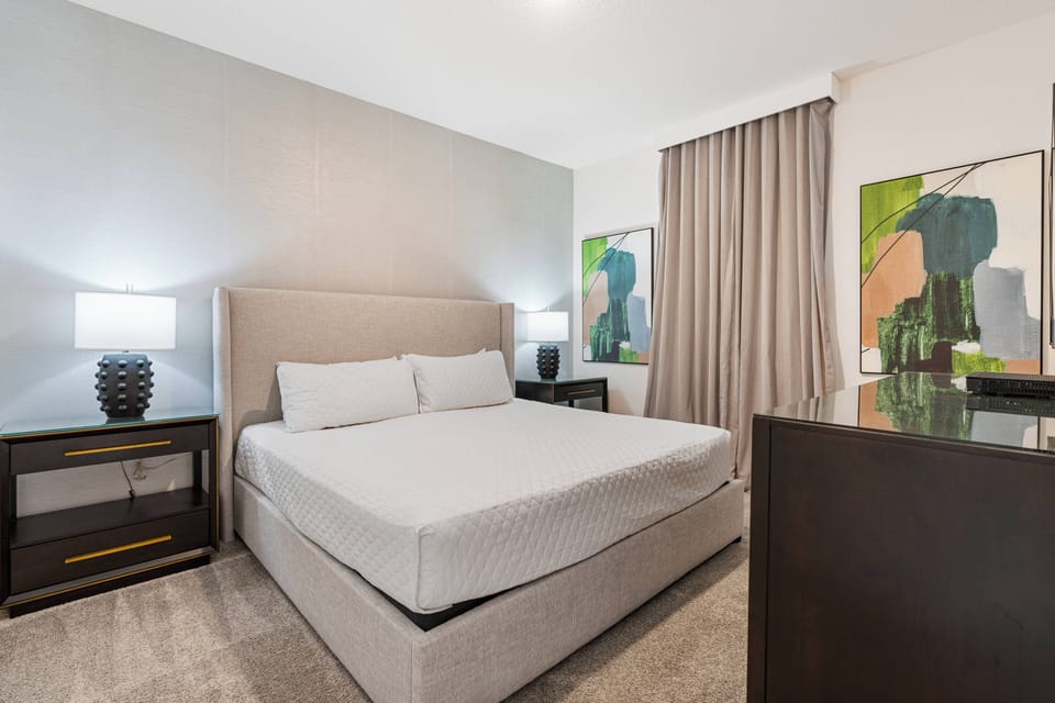 This stylish bedroom features a plush upholstered headboard that complements warm gray walls, with soft nightstand lighting creating a cozy ambiance and vibrant artwork adding color to enhance your relaxing stay.