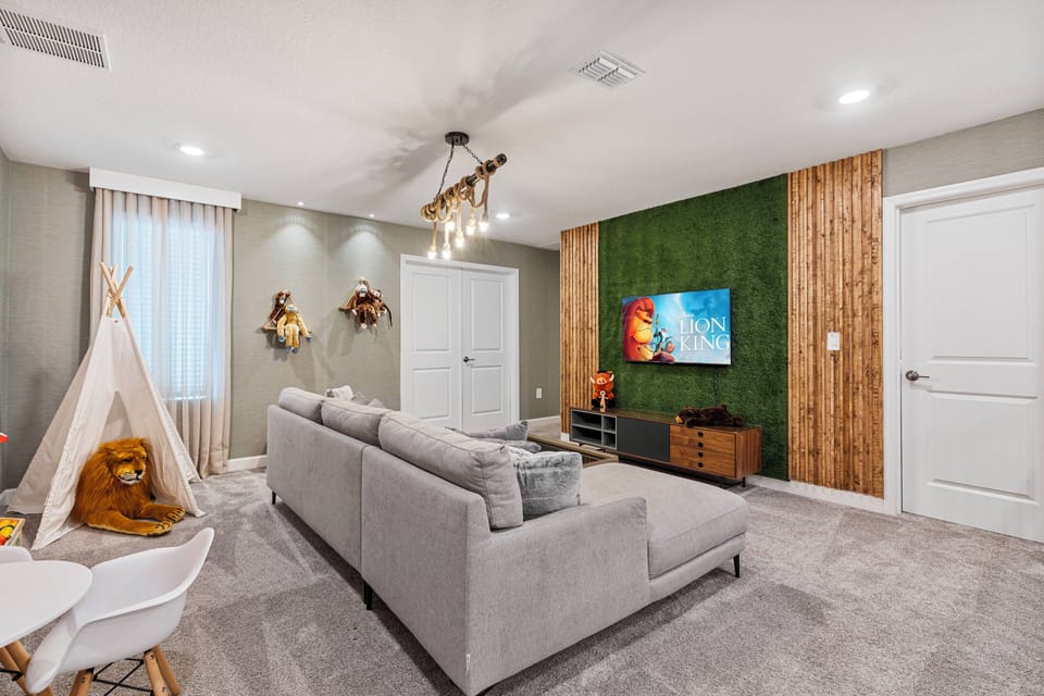 Welcome to a stylish living room where comfort and creativity blend, featuring a plush gray sofa, a vibrant green accent wall, and a cozy teepee for a playful touch, all enhanced by modern lighting for a relaxing atmosphere.