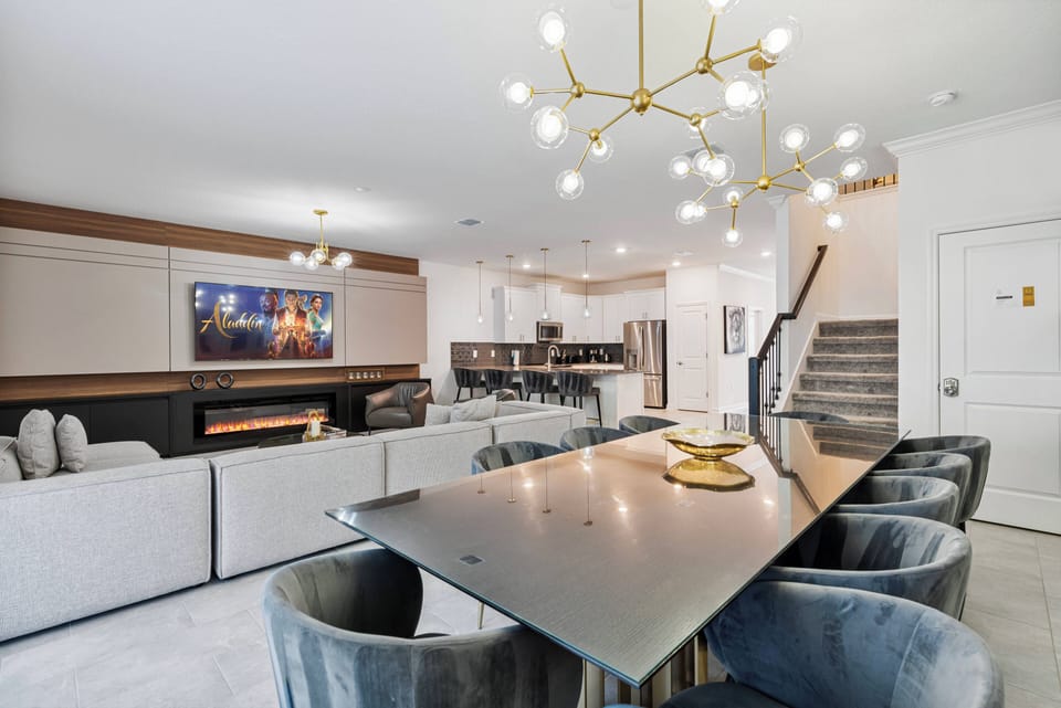 Step into a stylish dining area where a sleek black table is surrounded by plush, velvet chairs, perfect for shared meals. The modern chandelier casts a warm glow, complementing the inviting texture of the upholstered sofa nearby.