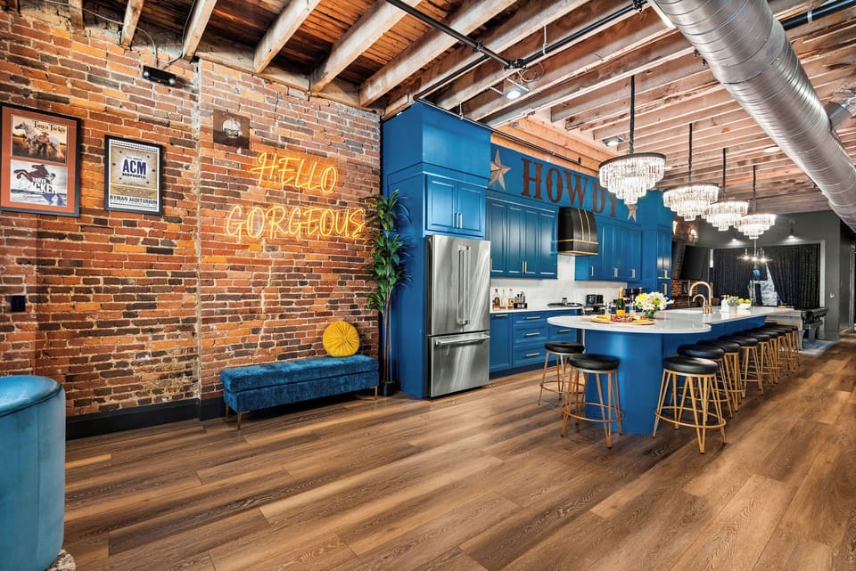 - Bright brick wall kitchen corner with neon Hello Gorgeous sign - Blue cabinetry long island and warm wood floors bring charm - Perfect open layout for cooking gathering and enjoying downtown life