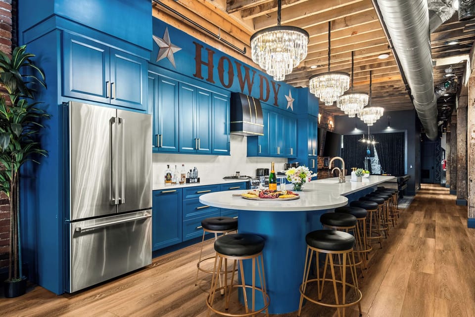 - Modern blue kitchen with long island seating and sparkling chandeliers - Stainless appliances and bold HOWDY signage set the vibe - Ideal cooking and dining space for groups in a stylish loft