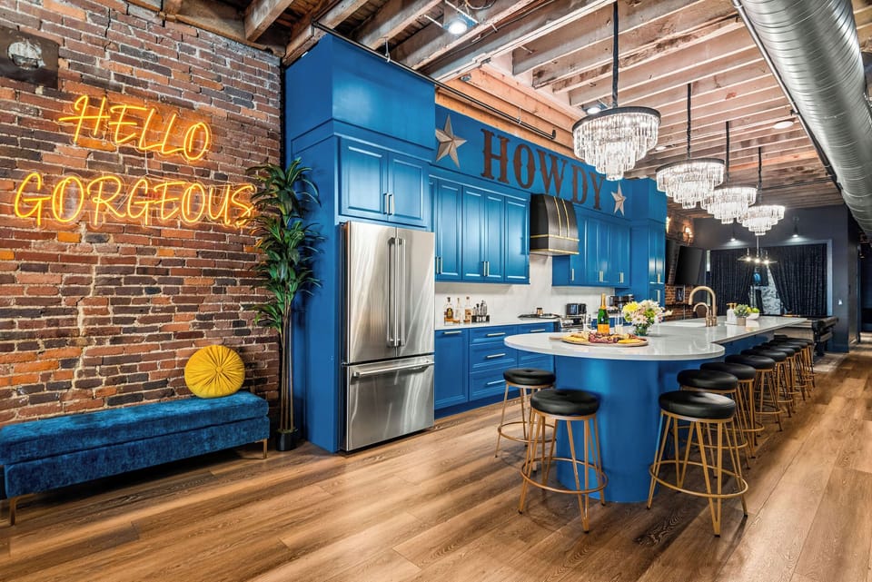 - Blue kitchen with island seating stainless appliances and modern lighting - Brick wall backdrop neon signs and chandeliers add vibrant character - Perfect cooking space for group stays in a trendy downtown loft