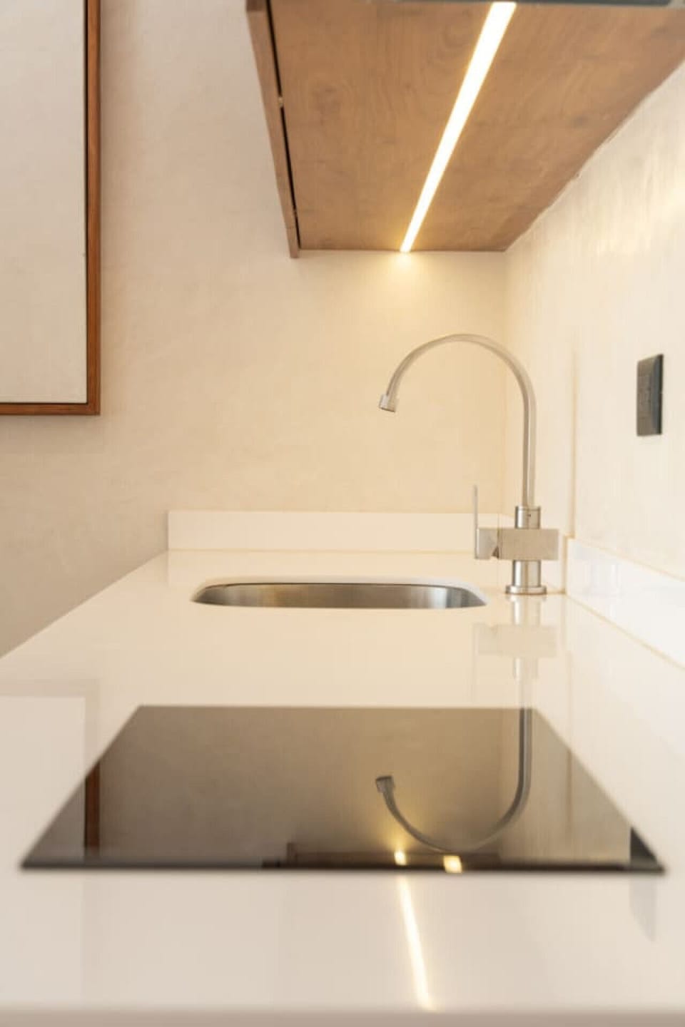 Minimalist kitchen with cooktop, sink, and warm lighting.