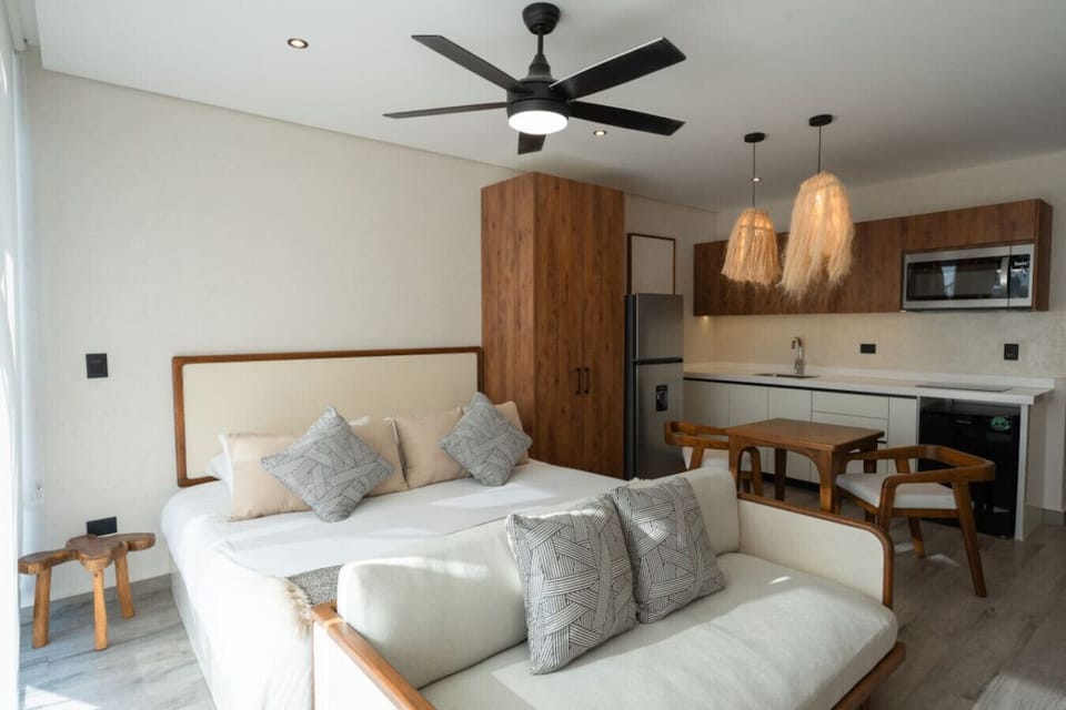 Cozy studio with kitchen, bed, sofa, and warm wood accents.