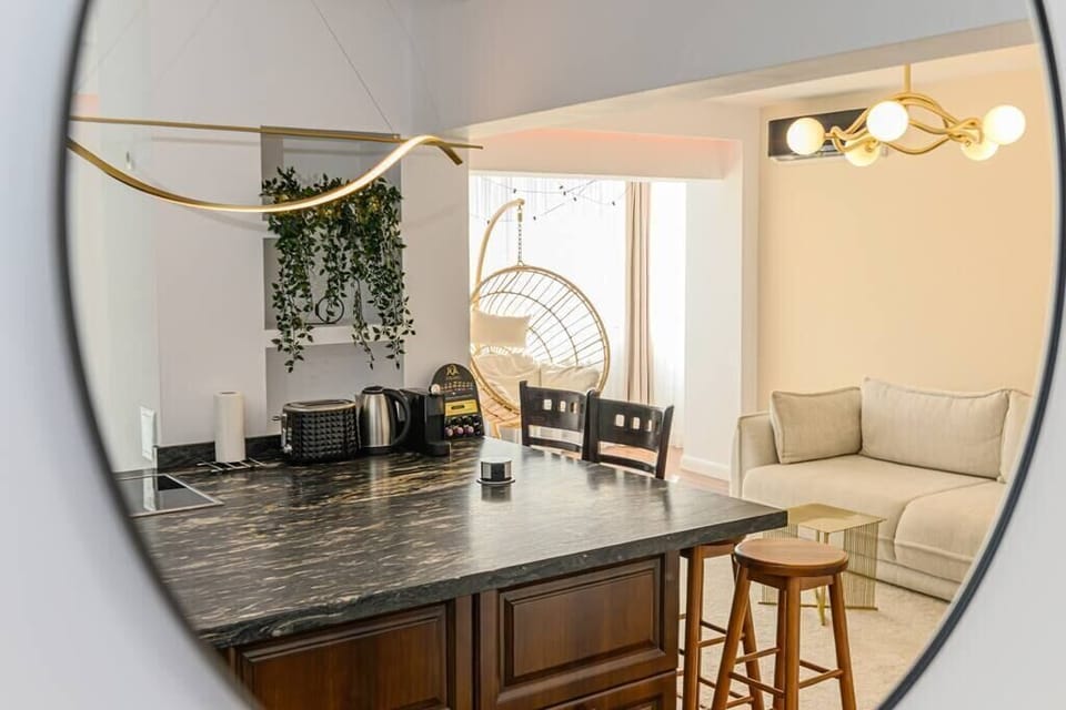Stylish living room featuring a huge extendable gray sofa, illuminating lamp, cozy chair with pillow on it, AC and internet connection, open space kitchen equipped with table and chairs for dining, toaster, coffee machine + capsules, kettle