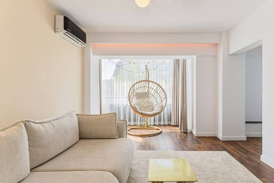 Stylish living room featuring a huge extendable gray sofa, illuminating lamp, cozy chair with pillow on it, AC and internet connection 