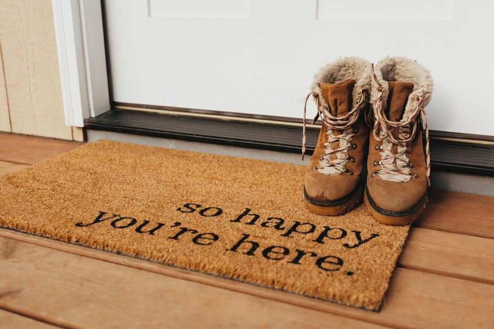 An inviting scene greets you at the entrance with a warm brown welcome doormat paired with rustic brown boots resting on a wooden floor, setting the tone for your adventure ahead.