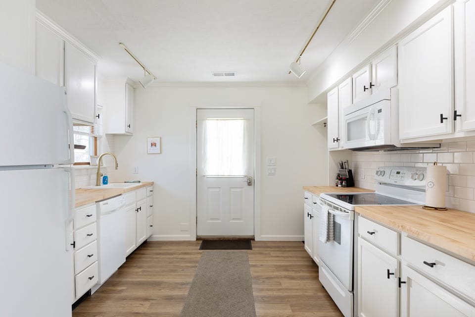 Long galley kitchen w/ white cabinets, wood counters & door to the outside