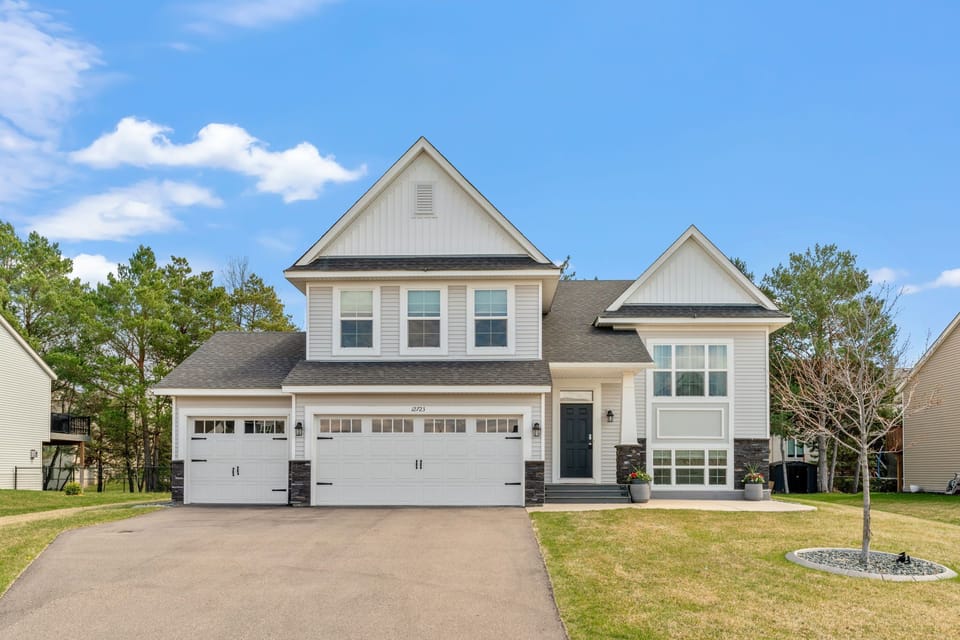 Modern two-story home with white siding, stone accents, and spacious three-car garage in peaceful residential neighborhood.