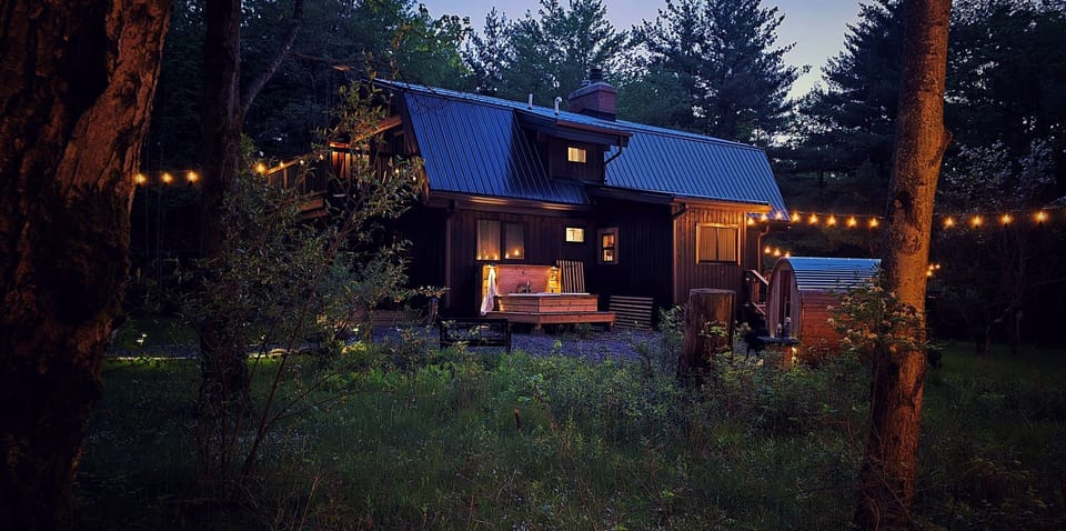Secluded outdoor spa tucked deep in the woods with a barrel sauna, soaking tubs, and peaceful nighttime views beneath the stars.