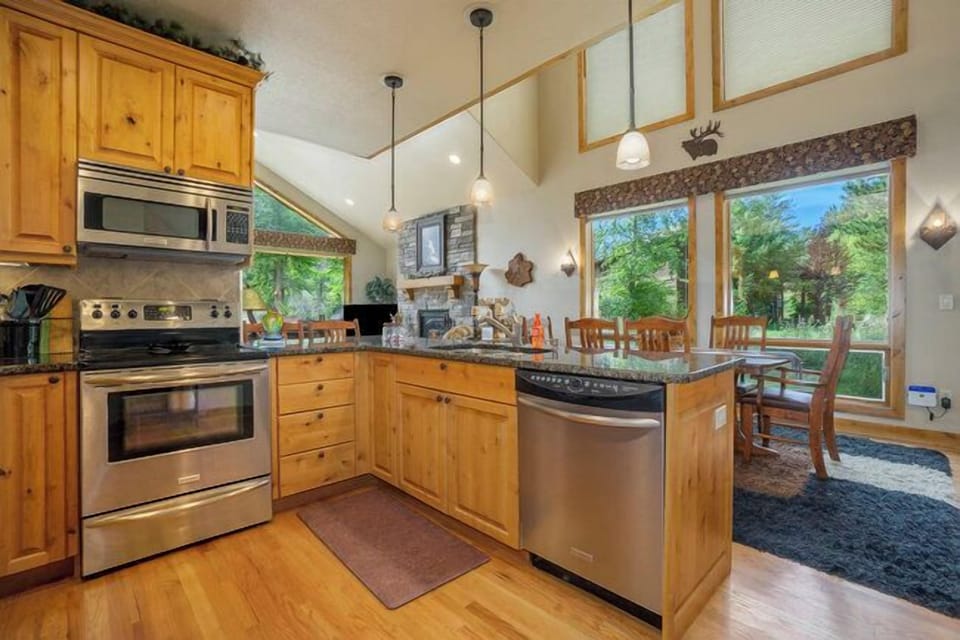 Moose River Cabin Kitchen with glass top electric stove/oven, with microwave range hood, and sink in the kitchen peninsula. Kitchen opens to dining area with rectangular dining table with seating for 6.