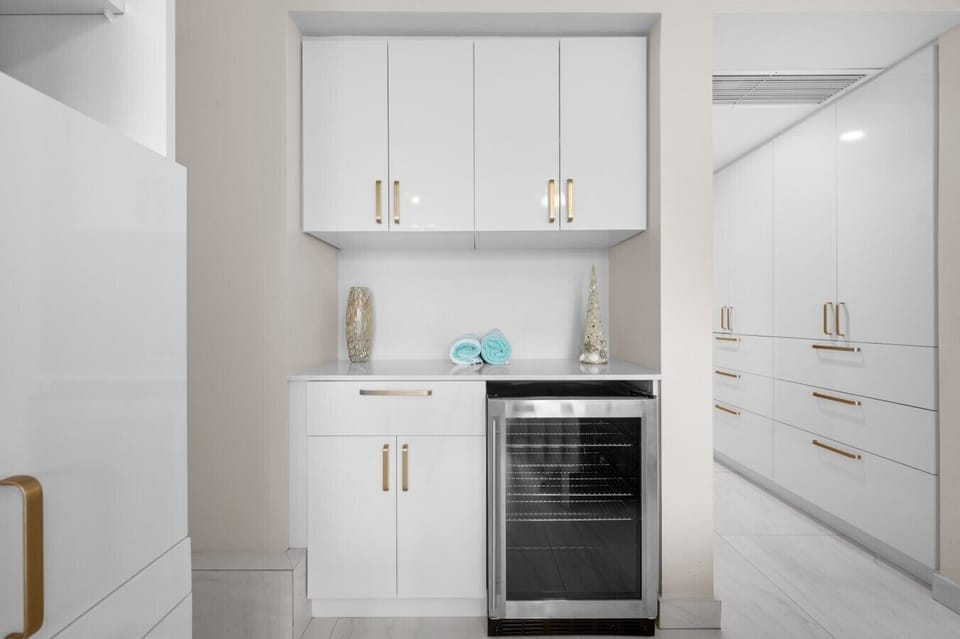 Sleek wet bar with beverage cooler and ample white cabinetry with gold accentsDSC_8916