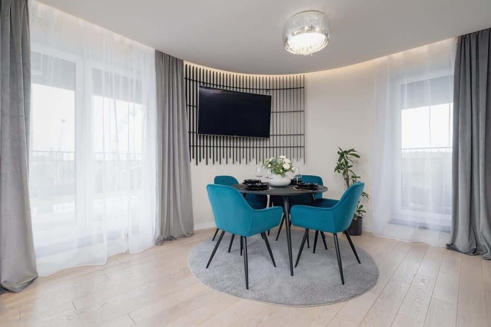 Dining area next to large windows, furnished with a black round table and teal velvet chairs.

