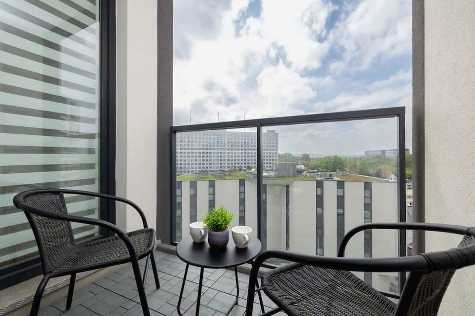 A private balcony setup with two chairs and a small round table, overlooking a cityscape.

