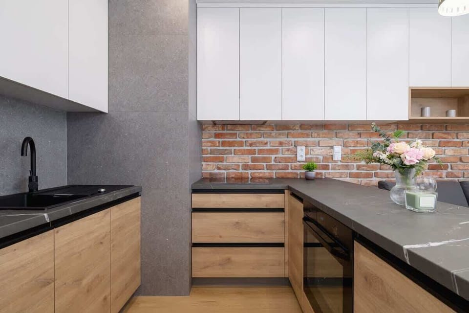 A minimalist kitchen with light and dark cabinetry, black countertops, and decorative flowers by the sink.

