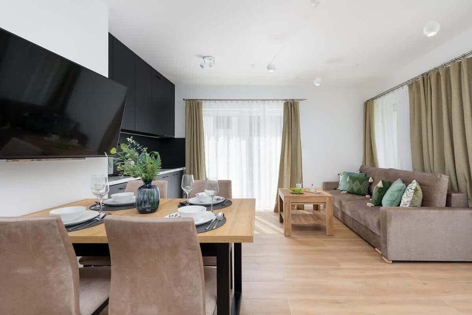A dining room area with a table set for a meal. A large TV hangs on the wall, and the room is open to the living area.