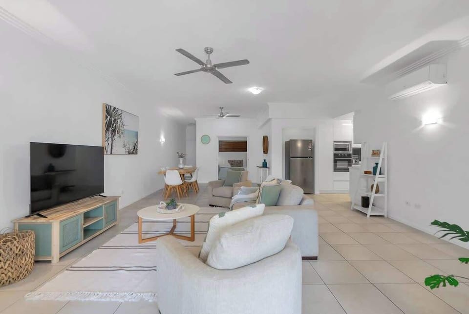 Relax in the chic, coastal-themed living room featuring a comfortable linen sofa, armchairs, and a central TV. 