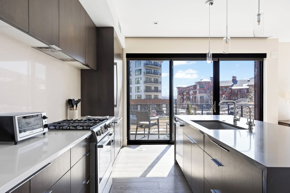 - Sleek kitchen with island sink and stainless appliances included  
- Sliding doors open to private balcony with resort and slope views  
- Bright natural light fills this modern cooking and dining space