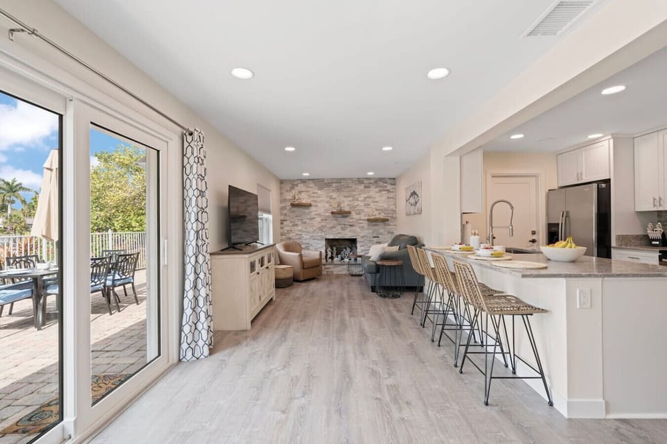 Florida living room with another large smart TV, 4 bar stools for additional seating, a loveseat and armchair.
