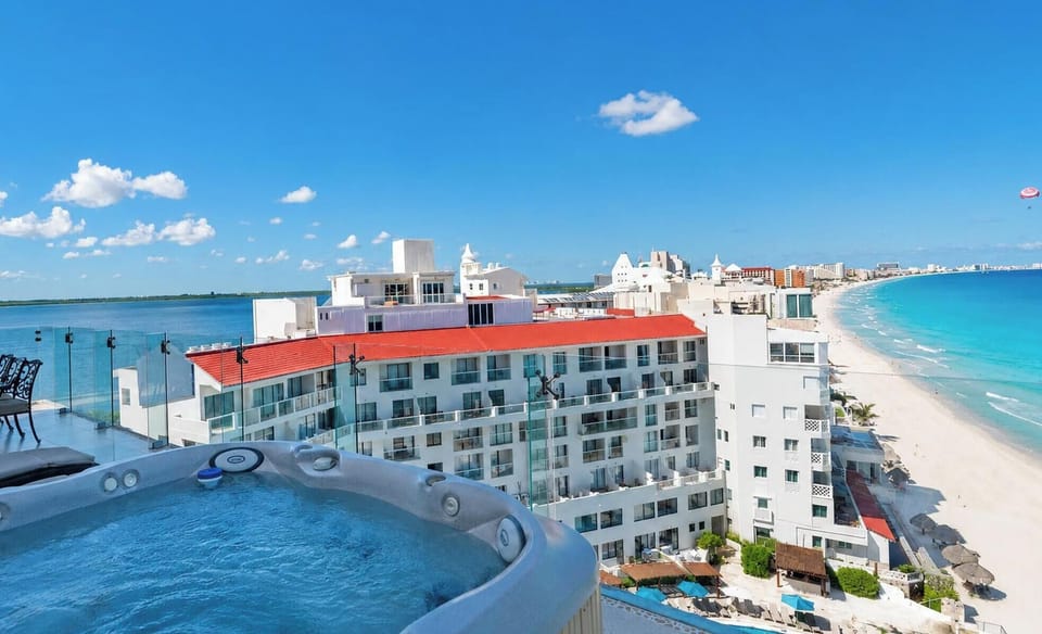 #323 - Penthouse Combo - 8 bedrooms, 6 baths sleeps 18 Rooftop hot tub bubbles beside glass railing, overlooking white sandy beach and turquoise ocean waters.