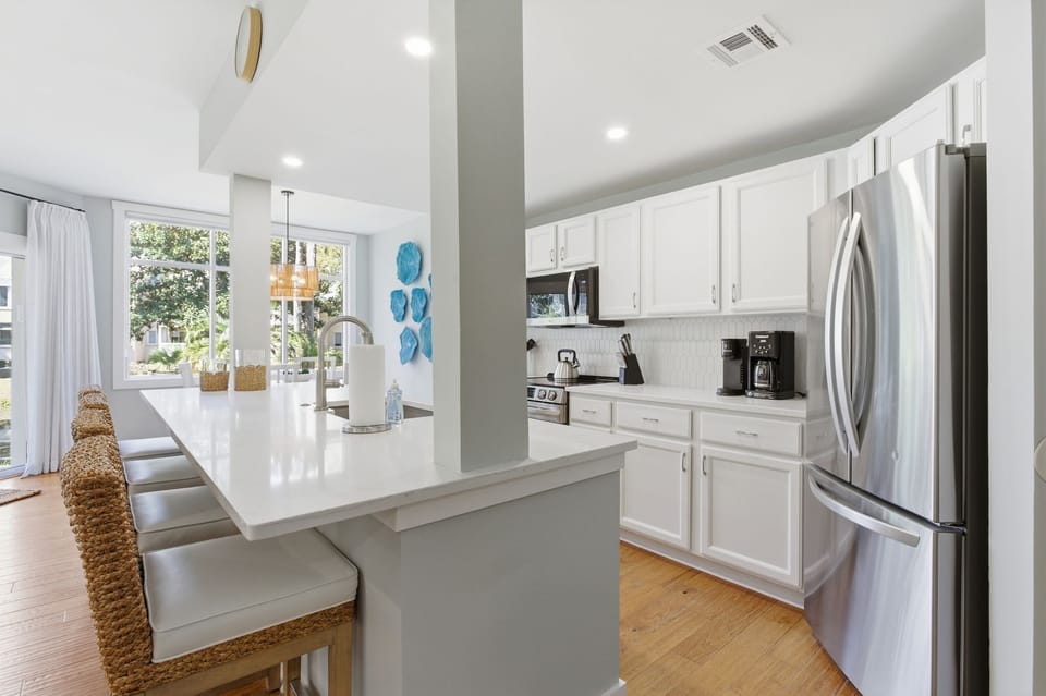 Your fully equipped kitchen features modern stainless steel appliances, pristine white cabinets, and a bright breakfast bar perfect for morning coffee.
