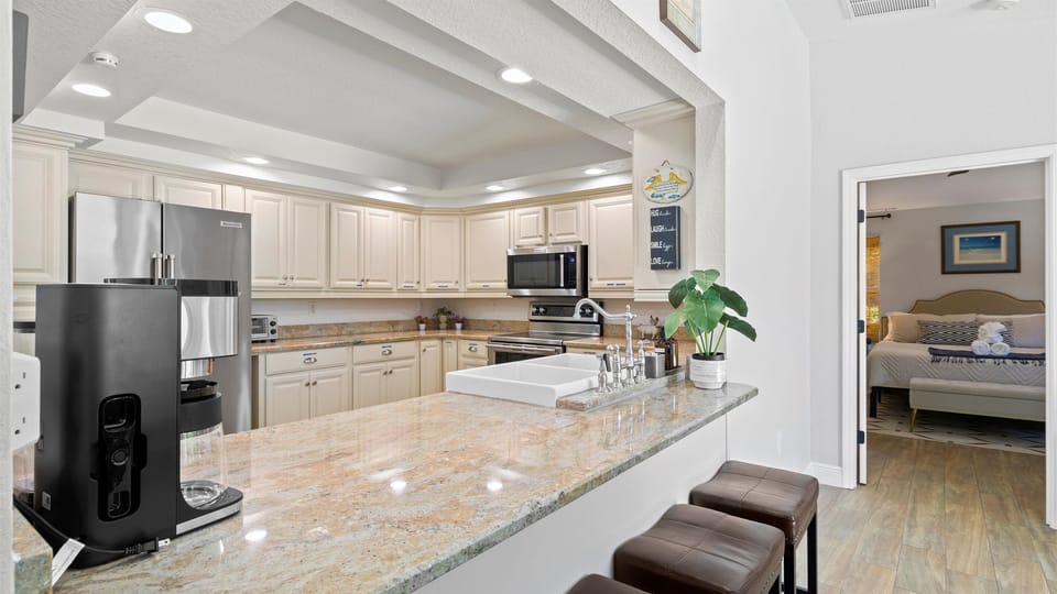 Bright and fully equipped kitchen with granite countertops, farmhouse sink, and coffee station—conveniently connected to a cozy bedroom retreat.
