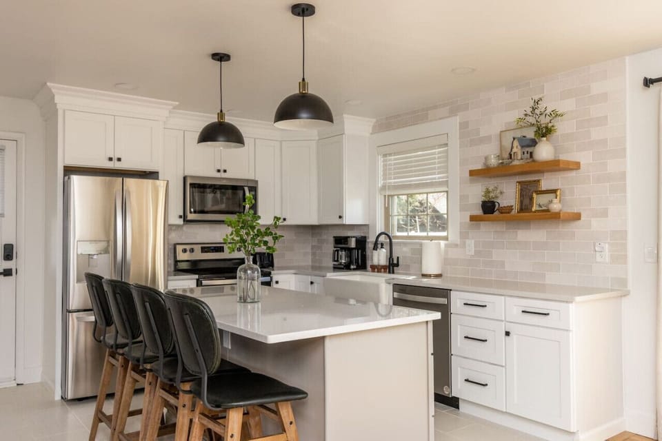 Modern kitchen w/ white cabinetry, stainless appliances & island seating for casual bites