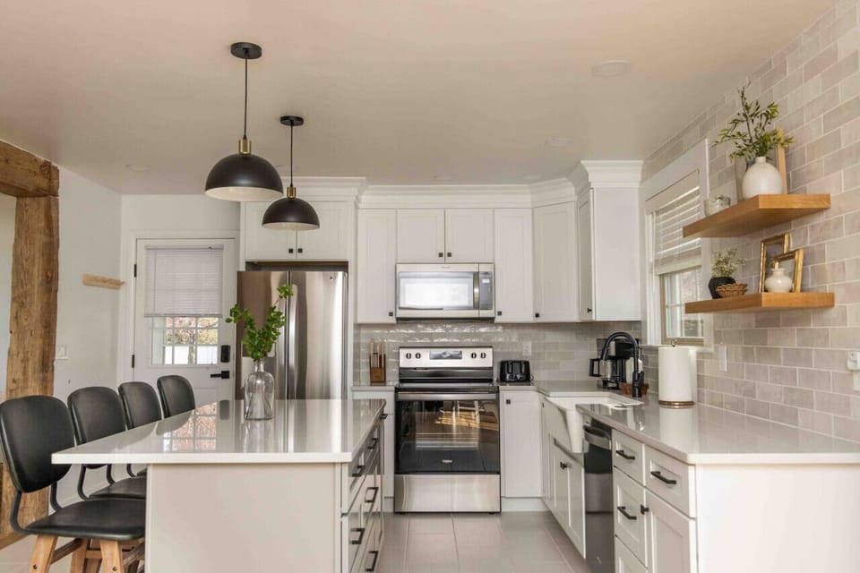 Bright kitchen w/ white cabinets, stainless appliances & island seating under pendant lights