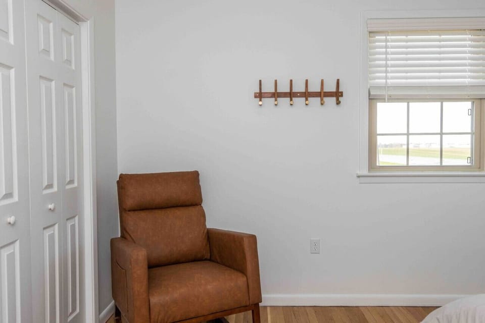 Simple bedroom corner w/ leather armchair, wall hooks & bright window views