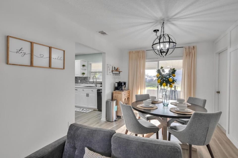Bright dining area with a round table, modern chandelier, and sunny backyard view.